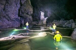 People in a cave with a light shining on the water Description automatically generated
